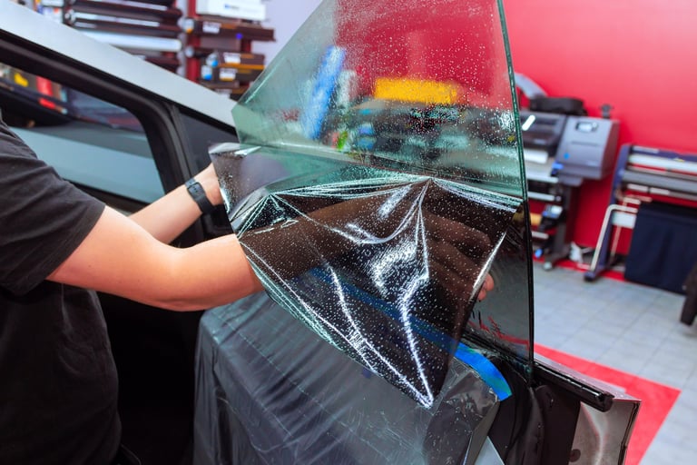 Worker applies tinted film to car window at workshop, showcasing meticulous window tinting installation